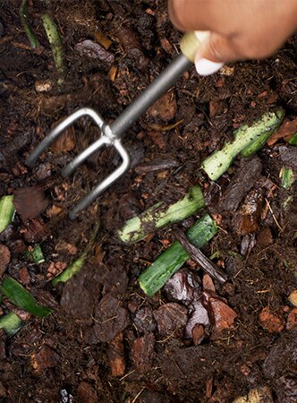 Mão mexendo na compostagem com uma ferramenta